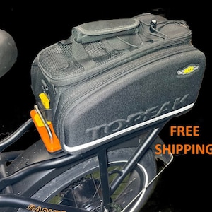 May include: Black Topeak bike pannier with a yellow buckle and the word "Topeak" printed in white on the side. The pannier is attached to a black bicycle.