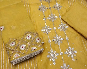 May include: A yellow fabric with a silver and white embroidered design. The fabric has a striped pattern and is decorated with small, round, mirrored embellishments.