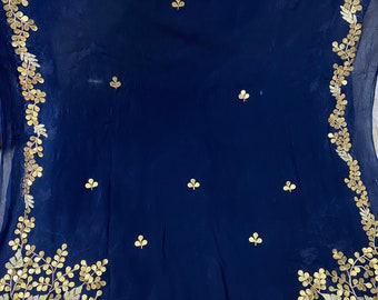 May include: A navy blue textile with gold leaf and clover embroidery. The gold embroidery forms a border along the edges and scattered clover designs across the fabric. The fabric has a slight sheen.