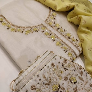 May include: A white cotton kurta with yellow and gold embroidery. The kurta is paired with a matching yellow dupatta and a small white embroidered pouch.