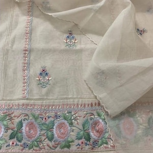 May include: White sheer fabric with delicate floral embroidery in shades of pink, blue, and green. The embroidery features a repeating pattern of flowers and leaves.