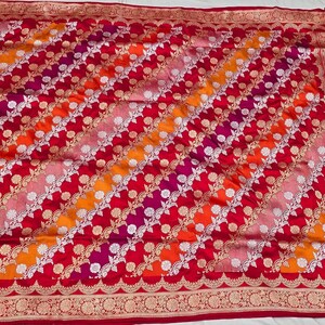 May include: A red, orange, pink, and white patterned silk saree with a gold border. The saree has a traditional Indian design.
