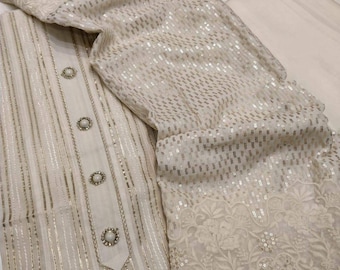 May include: A white and gold embroidered dress with sequins. The dress has a long sleeve and a high neck. The fabric is sheer and has a delicate pattern.