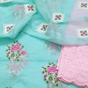 May include: A turquoise fabric with pink floral embroidery. The fabric has a sheer, net-like texture. A pink fabric with a scalloped edge is visible in the bottom right corner.