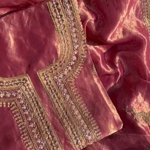 Puede incluir: Una tela rosa transparente con bordados dorados y plateados. La tela tiene una textura delicada y brillante.