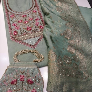 May include: A green embroidered fabric with a matching green fabric with a gold pattern. The fabric is decorated with pink and white flowers and beads. A small green purse with pink and white flowers and beads is also included.