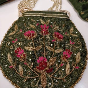 Może przedstawiać: Oliwkowo-zielona, ​​koralikowa torebka z kwiatowym wzorem. Torebka posiada różowe kwiaty, złote hafty i koralikową rączkę. Krawędzie są obszyte złotymi koralikami, a torebka ma perłowy pasek.