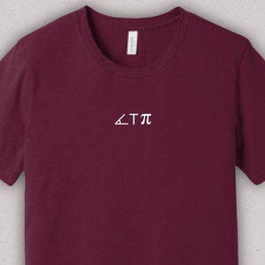 Puede incluir: Una camiseta color burdeos con un gráfico blanco que dice "<Tπ".