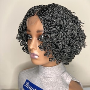 Puede incluir: Una peluca negra trenzada con extremos rizados. La peluca está en una cabeza de maniquí con una camisa gris que dice "Beauty hub, we make you look gorgeous and confident, long lasting handmade".