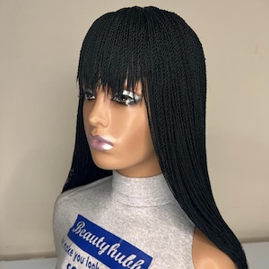 May include: Black micro braid wig with a fringe. The wig is styled in long, thin braids and has a straight, blunt fringe. The wig is worn by a mannequin with a grey shirt that says "Beautyhulla make you look gorgeous and confident long lasting handmade wigs".