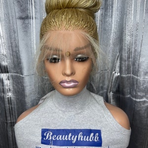 May include: A blonde wig styled in a high bun, displayed on a mannequin head. The wig features a lace front and a natural-looking hairline. The mannequin is wearing a gray top with the text "Beauty hubb" and the slogan "we make you look gorgeous and confident".