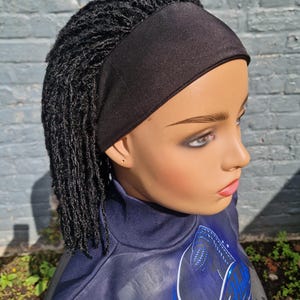 Puede incluir: Una cabeza de maniquí con una diadema negra y extensiones de micro-locs negras adjuntas. El maniquí tiene una tez clara y suave, y viste una prenda azul oscuro de cuello alto con el texto Beauty Hub y You Look Gorgeous.