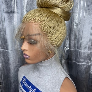 May include: A blonde braided wig styled in a high bun, displayed on a mannequin head. The wig features a lace front and is made of small, tightly woven braids. The mannequin is wearing a gray sleeveless top with the text "Beauty hubble".