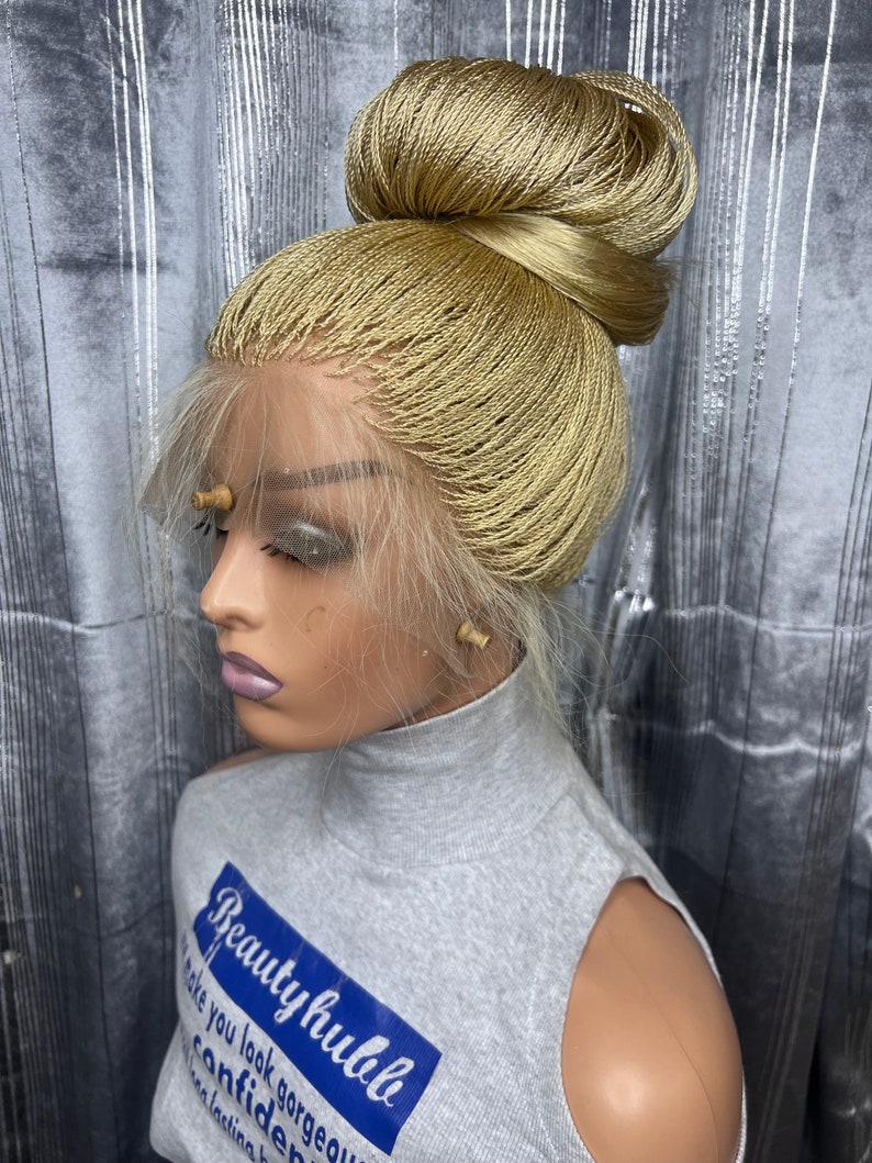May include: A blonde braided wig styled in a high bun, displayed on a mannequin head. The wig features a lace front and is made of small, tightly woven braids. The mannequin is wearing a gray sleeveless top with the text "Beauty hubble".