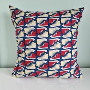 May include: A blue square pillow with a pattern of red and cream sneakers. The sneakers are arranged in a repeating pattern.