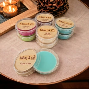 May include: Assortment of six small round wax melts in clear containers with brown paper labels. The labels have the text "Wilson & Co." and the scent name. The scents are Summer Fruits, Sweet Vanilla, Bliss Unstoppable, Chocolate Orange, and Fresh Linen.