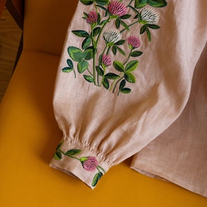 May include: A pale pink linen blouse with embroidered clover flowers in shades of green and pink.