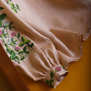 May include: A beige linen blouse with embroidered clover flowers in shades of green and pink.
