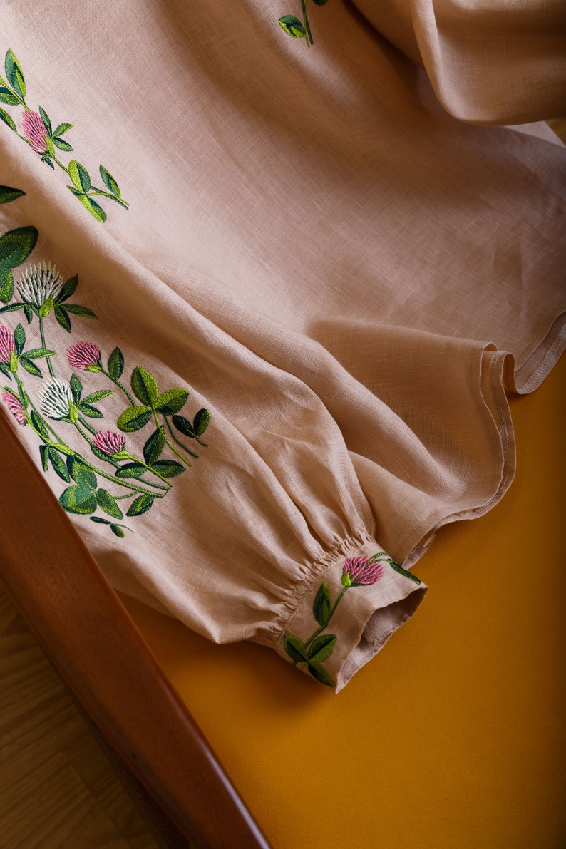 May include: A beige linen blouse with embroidered clover flowers in shades of green and pink.
