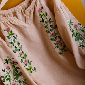 May include: A beige linen blouse with embroidered clover flowers in shades of green, pink, and white.