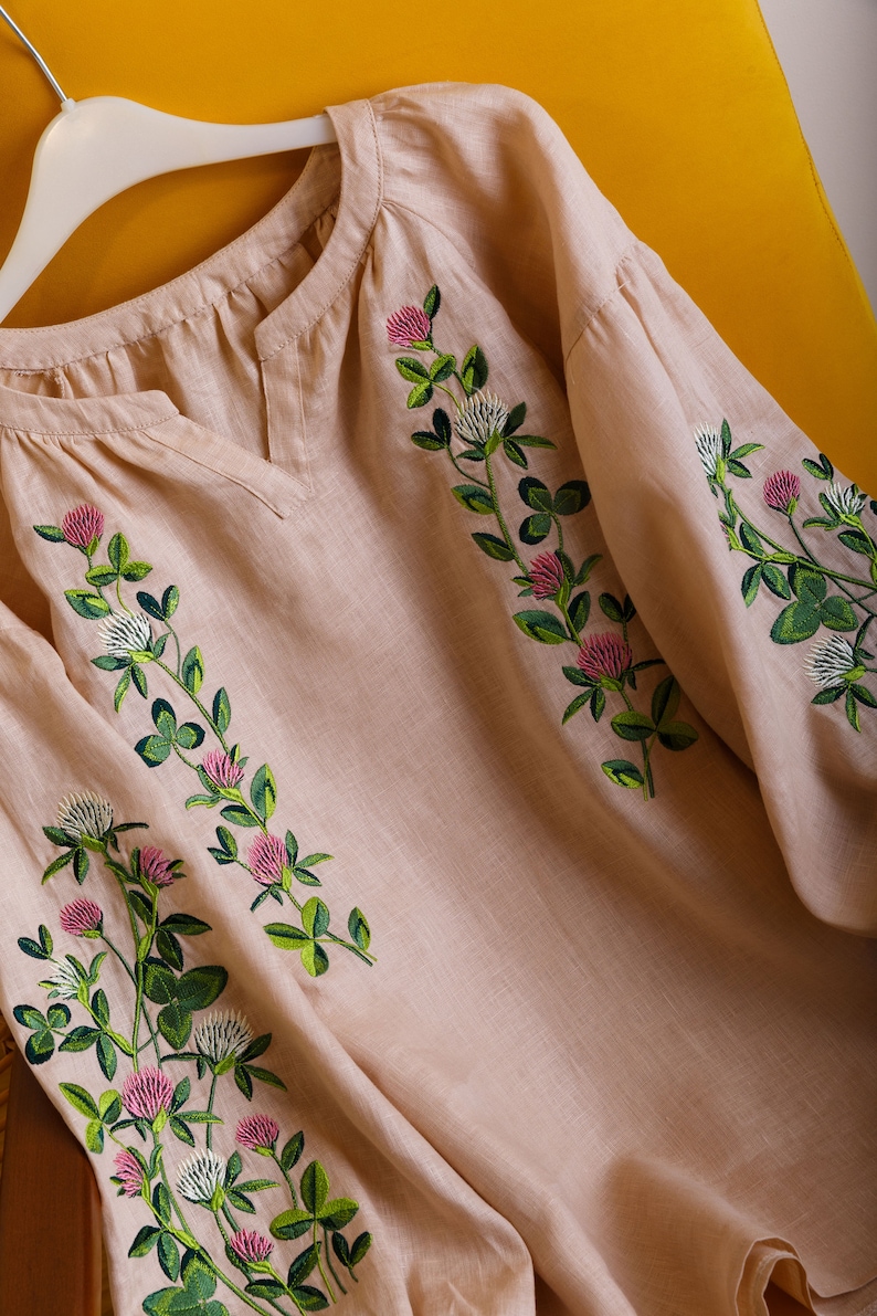 May include: A beige linen blouse with embroidered clover flowers in shades of green, pink, and white.