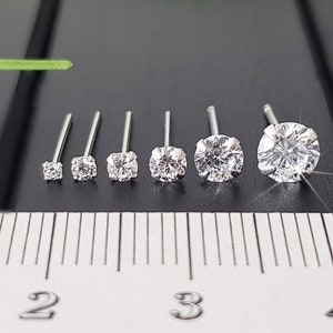 Puede incluir: Siete tachuelas de nariz de plata con piedras redondas de circonita cúbica transparentes de diferentes tamaños. Las piedras están alineadas en una regla con los números 2, 3 y 4 visibles.