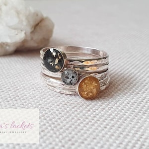 Op de afbeelding: Een set van vier zilveren stapelringen met kleine ronde harsinlegsels. De harsinlegsels zijn zwart met gouden vlokken, grijs met gouden vlokken en goud met zwarte vlokken.