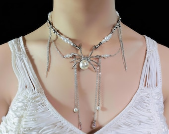 May include: Silver-toned spider necklace with a pearl body and dangling chains. The necklace features a choker style with faux pearls and a spider pendant. The chains have small pearls and pink accents.