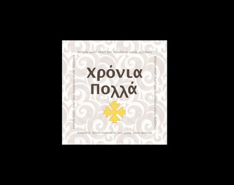 May include: A white card with a brown swirl pattern and the text "Χρόνια Πολλά" in brown lettering. A yellow cross is in the center of the card.