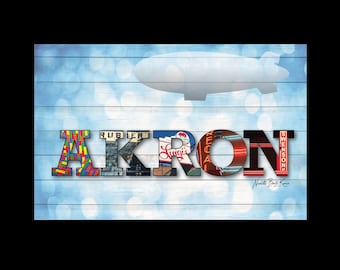May include: A digital art print featuring the word "AKRON" in colorful, textured letters against a light blue wood-grain background. A blimp silhouette floats above the word, with a bokeh effect.