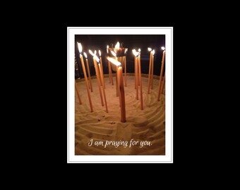 May include: A group of lit candles arranged in a circle on a sandy surface. The candles are all the same size and shape, and they are burning brightly. The text "I am praying for you" is written below the candles.