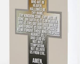 May include: A beige card with a cross-shaped design featuring the Lord's Prayer in black text. The cross is decorated with olive branches and a dark brown background. The text "AMEN" is at the bottom of the card.