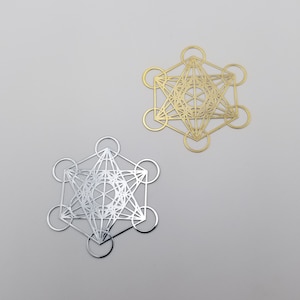 May include: Two geometric metal ornaments in the shape of a star with a circle around each point. The ornament on the left is silver and the ornament on the right is gold.