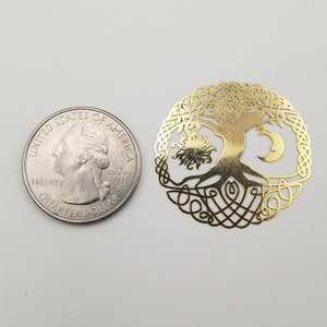 May include: Gold-colored metal tree of life pendant with a sun and moon design. The pendant is about the size of a US quarter.