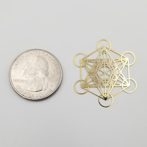 May include: Gold-colored metal geometric shape with a detailed design, similar in size to a US quarter.