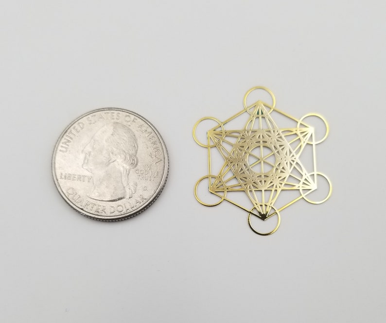 May include: Gold-colored metal geometric shape with a detailed design, similar in size to a US quarter.