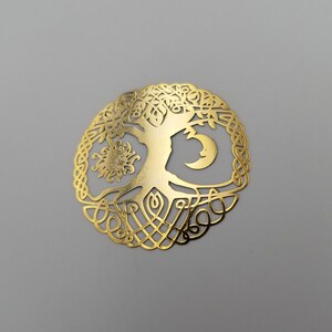 May include: A gold-colored metal tree of life pendant with a sun and moon design. The tree is intricately detailed with branches and roots.