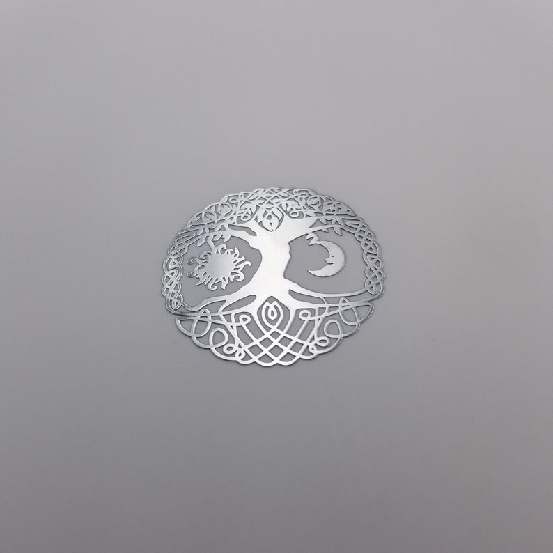 May include: A silver metal tree of life pendant with a sun and moon design. The tree is surrounded by intricate knotwork.