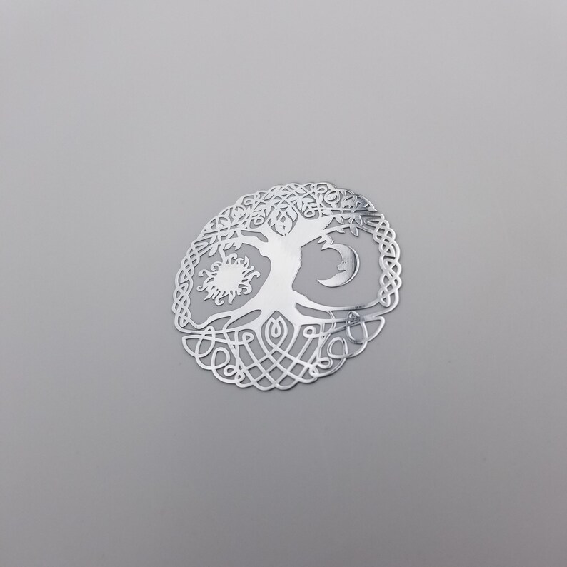 May include: Silver-toned metal tree of life pendant with a sun and moon design. The tree is intricately detailed with a Celtic knot border.