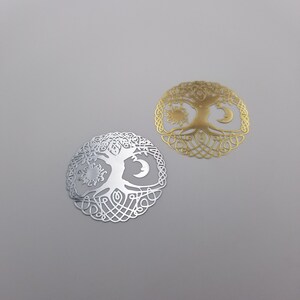 May include: Two metal tree of life charms, one silver and one gold, with a sun and moon design.