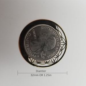 May include: A gold-colored metal coin charm with a decorative design featuring a circle of flower-like shapes. The charm is 1.25 inches in diameter and features a United States quarter dollar coin inside. The coin has the words "UNITED STATES OF AMERICA", "LIBERTY", "IN GOD WE TRUST", and "QUARTER DOLLAR" inscribed on it.
