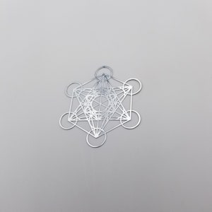 May include: A silver metal pendant featuring a geometric design with a star shape in the center. The design is intricate and includes multiple overlapping circles and lines.