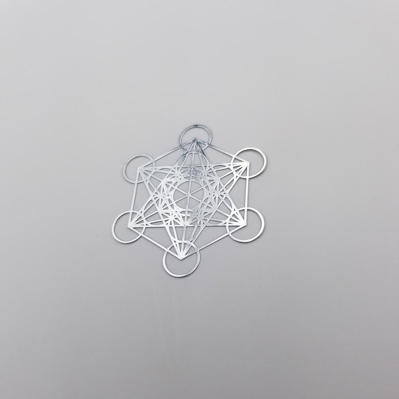 May include: A silver metal pendant featuring a geometric design with a star shape in the center. The design is intricate and includes multiple overlapping circles and lines.