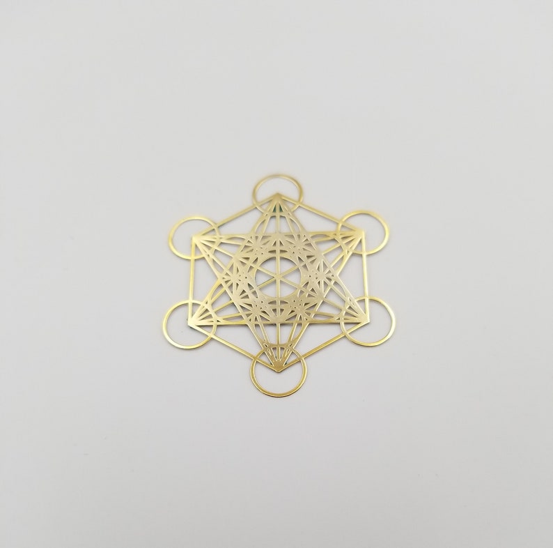 May include: A gold-colored metal pendant featuring a geometric design with a star shape in the center. The design is intricate and detailed, with multiple lines and circles.