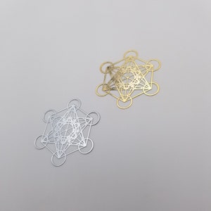 May include: Two geometric metal shapes, one silver and one gold, with a complex pattern of overlapping circles and lines. The shapes are similar in design and appear to be made of thin metal.