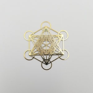 May include: Gold-colored metal geometric design with a circular pattern in the center. The design is a combination of squares, triangles, and circles.