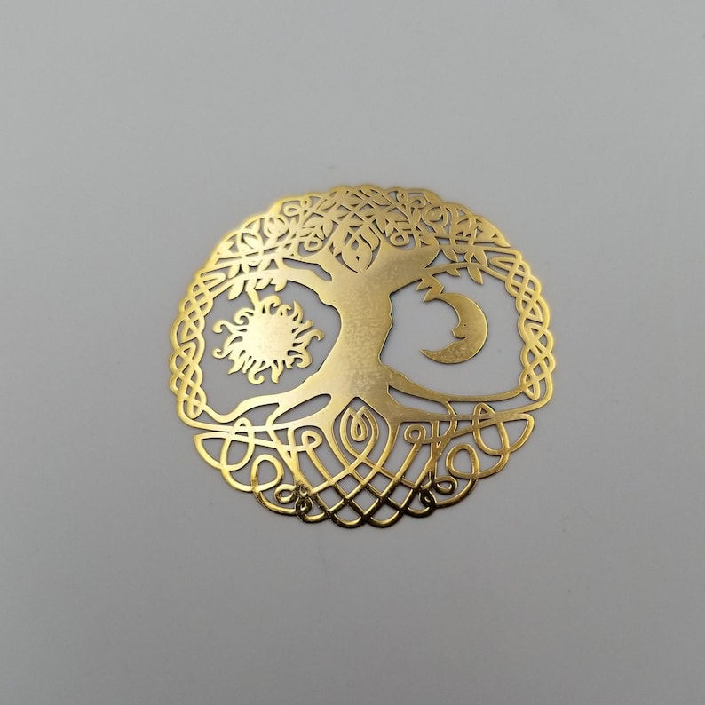 May include: A gold metal tree of life ornament with a sun and moon design. The tree is surrounded by a Celtic knot pattern.