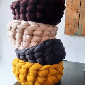 May include: Four knitted baskets stacked on top of each other. The baskets are brown, beige, gray, and yellow.