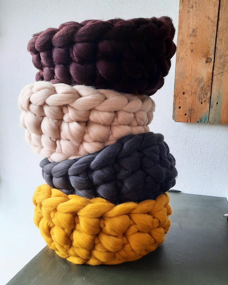 May include: Four knitted baskets stacked on top of each other. The baskets are brown, beige, gray, and yellow.