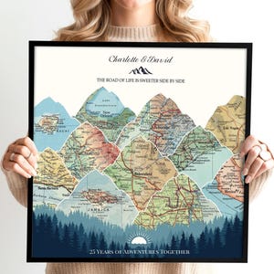 May include: A framed map art print featuring a mountain range design. The mountains are composed of vintage map sections, with a forest scene at the base. The text reads "Charlotte & David" and "25 YEARS OF ADVENTURES TOGETHER."